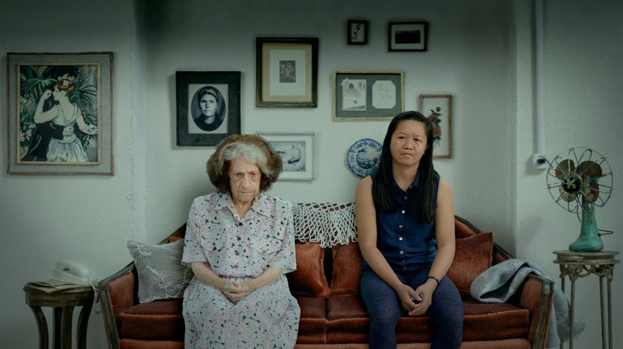 Two women sit on a couch. Photos on the wall