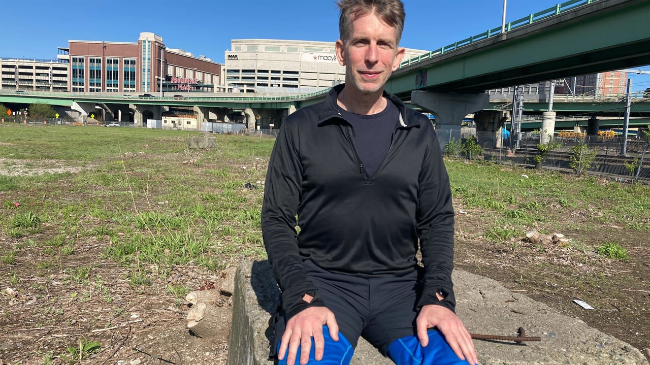 Man sits by a raised highway in a grass field