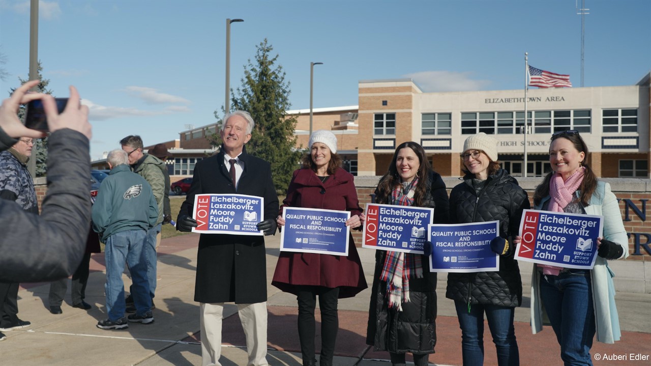 Five people stand holding signs encouraging voting