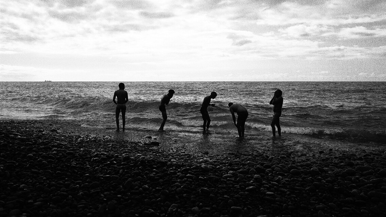 Five people on the shore of a pebbled beach