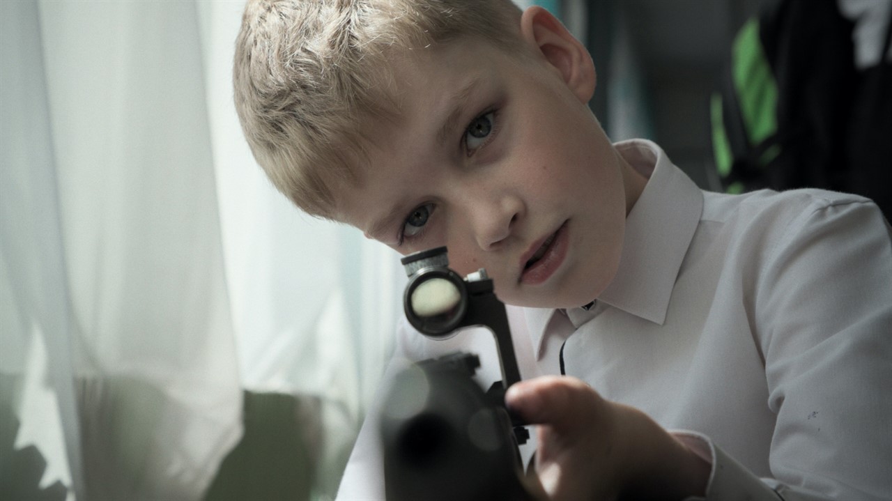 A young boy looks down the scope of a rifle