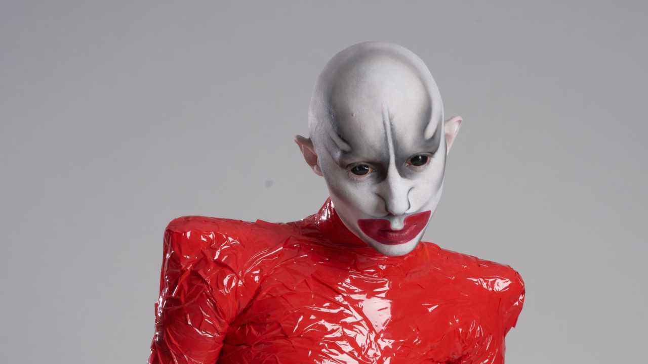 a person with elaborate makeup and a red PVC suit