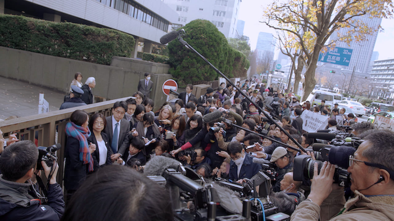 Crowd of reporters outside around a group of three